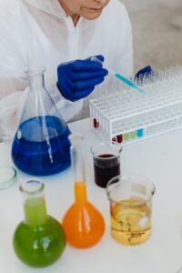 woman in blue gloves filling test tubes with colorful liquids using a dropper